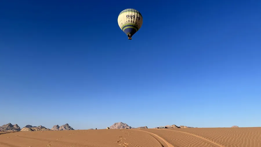A single hot air balloon in a clear blue sky above the dunes