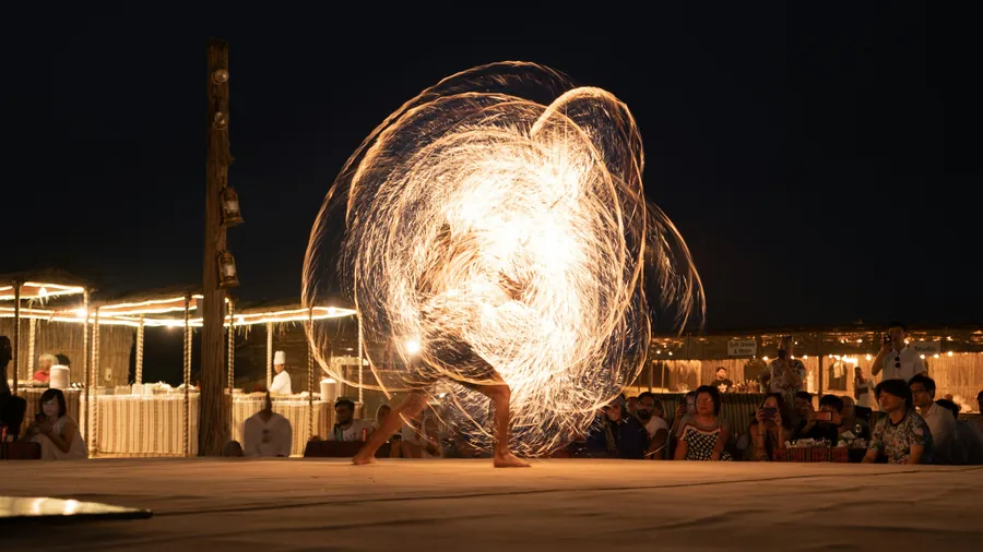 A fire performer spinning flames at a desert camp at night