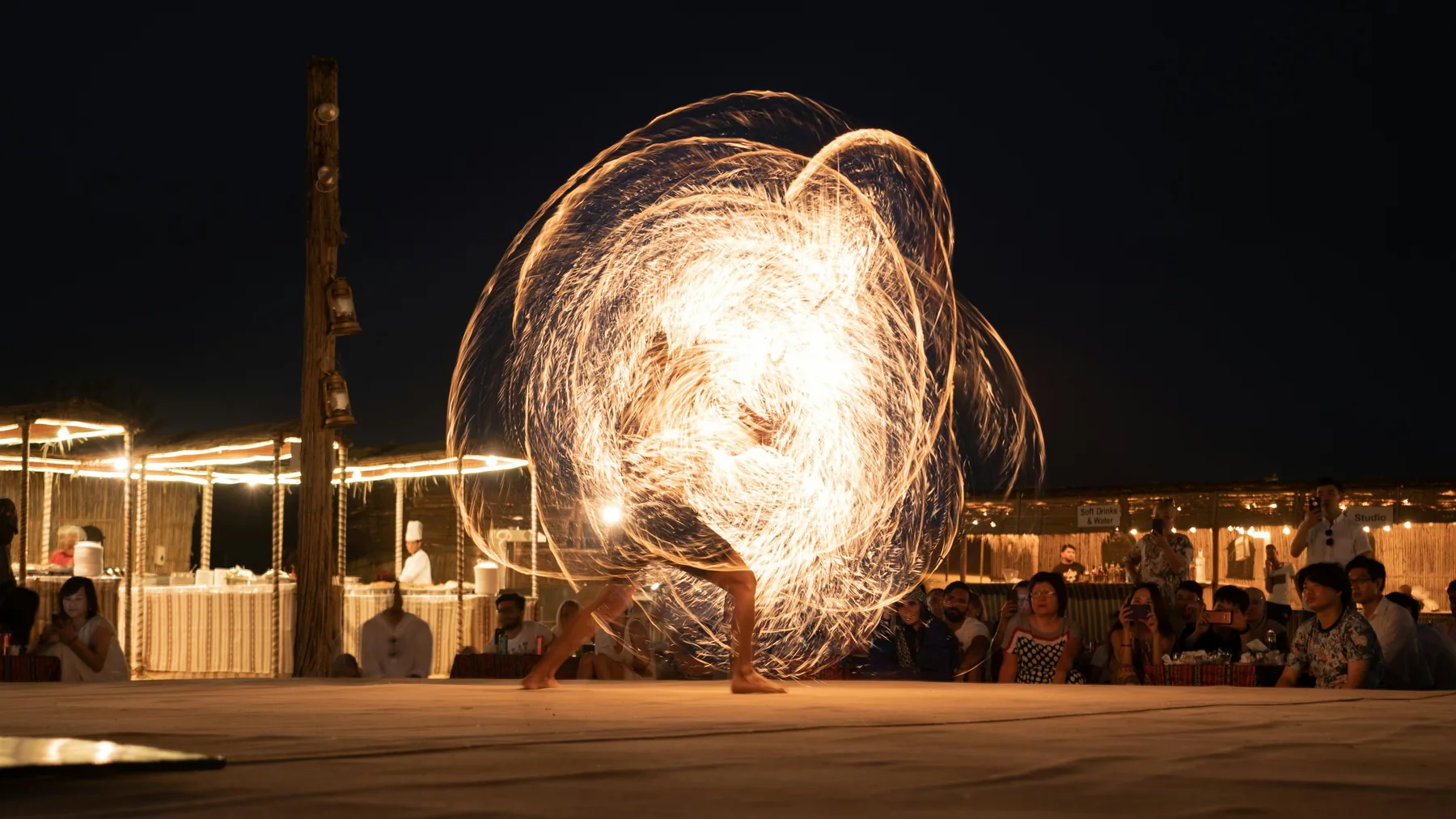 A fire performer spinning flames at a desert camp at night