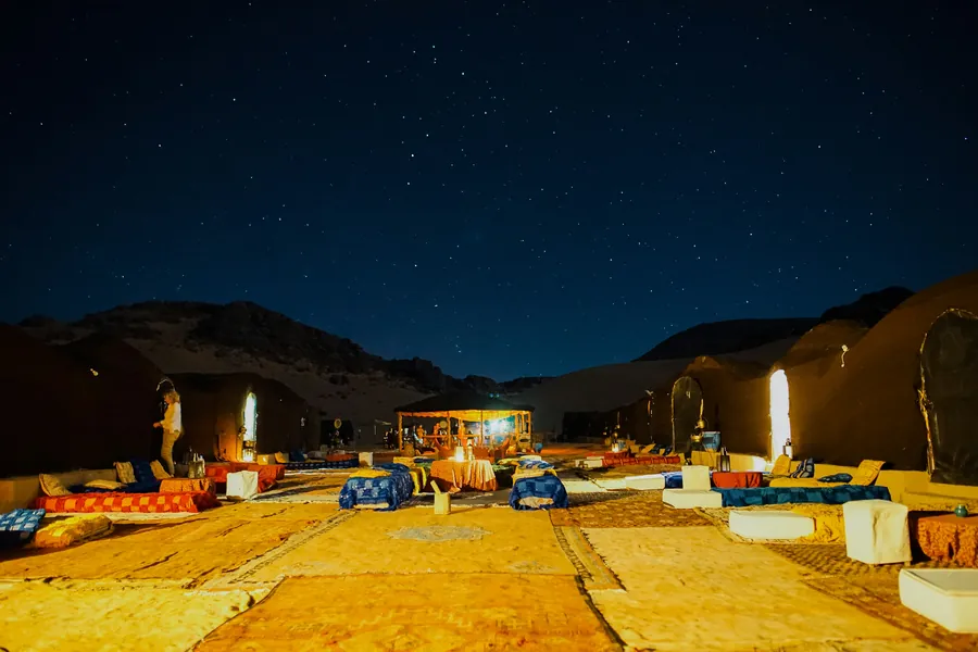 A lantern-lit desert camp with floor seating under a starry sky