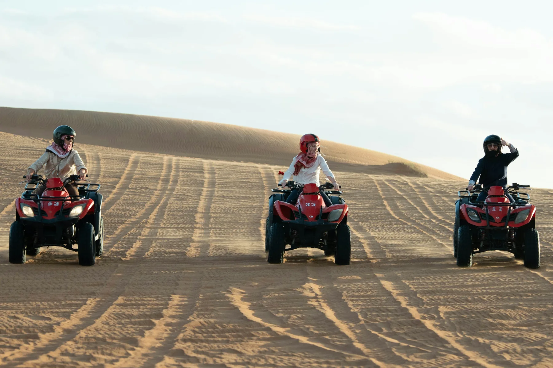 Three riders on red quad bikes in the desert