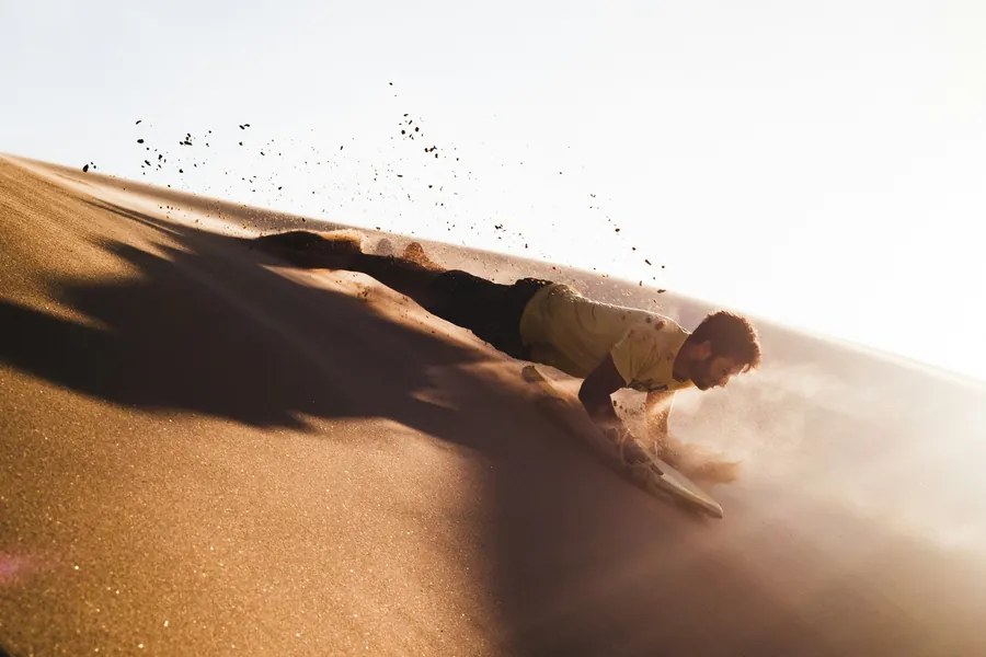 A sandboarder sliding down a steep dune